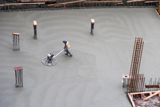 Canada, BC, Vancouver.  Construction worker using a power trowel to smooth the surface of concrete slab floor in building foundation.