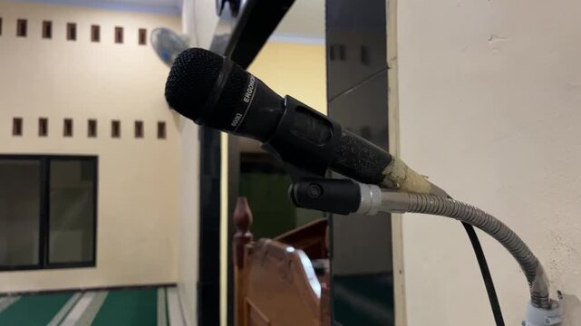Close up of mosque azan microphone mounted on pulpit indoors. Audio equipment used for sermon and prayer call, creating solemn, focused, and spiritual atmosphere.
