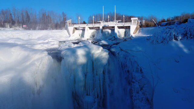 Winter drone video soaring above the frozen waterfall of the Mitis-1 hydroelectric dam on the Mitis River. Gaspe Peninsula, Price, Quebec, Canada, 2026.
