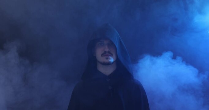 Man in hood going into smoke on dark background with blue light