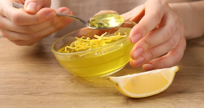 Woman eating tasty lemon jelly with zest at wooden table, closeup