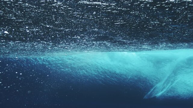 Underwater barrel wave forming smooth blue arc with bubbles and soft ambient light