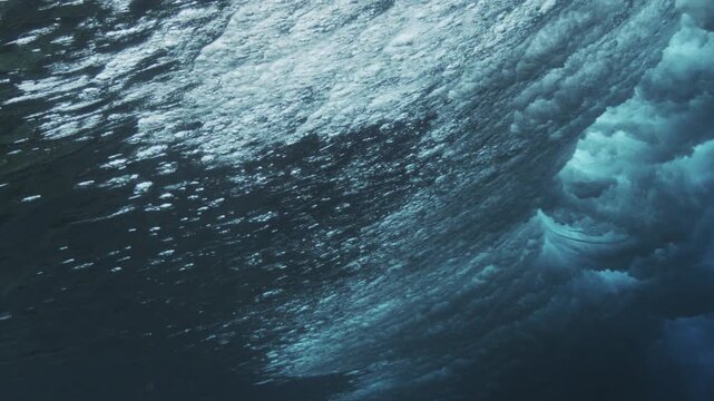 Breaking underwater wave with scattered bubbles and glowing light forming abstract ocean texture