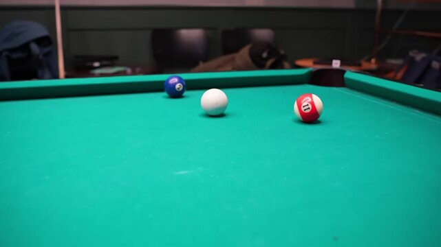 Close-up pool table scene with cue ball, blue 2 and red striped 11 near a corner pocket on green felt, shallow depth of field in a bar lounge.