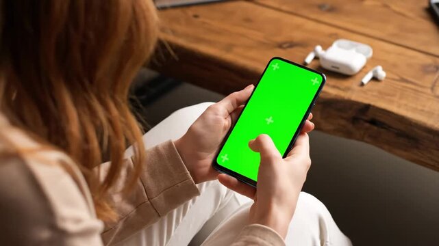 Woman's hands interacting with a smartphone featuring a green screen for custom content display or app mockup.