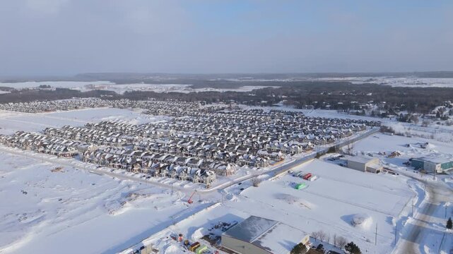 Aerial drone view of snow covered new housing development in Erin Ontario, showing large residential neighborhood, rows of modern houses, winter streets, and expanding suburban community
