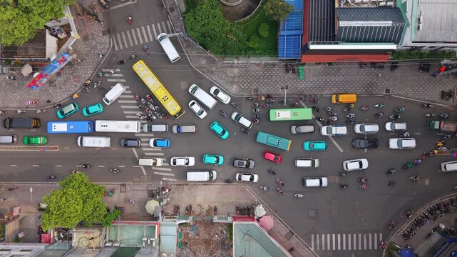 Top-down drone view of dense traffic at busy urban intersection in Ho Chi Minh City. Cars, buses and motorbikes create organized chaos typical of fast-growing Southeast Asian cities.