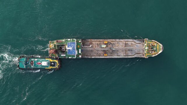 Tugboat pushing large cargo barge aerial top down view
