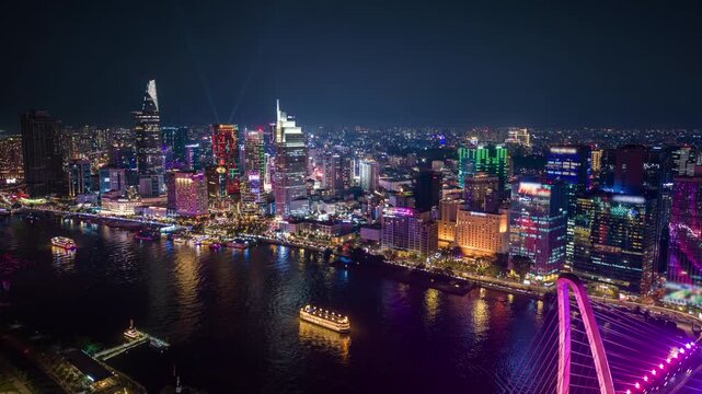 Aerial night timelapse of Ho Chi Minh City skyline with illuminated bridge, river reflections, and vibrant city lights. Modern urban landscape of Vietnam financial district.