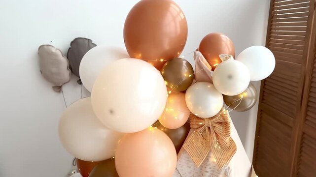 Kids teepee decorated with white, beige and brown balloons and a fairy lights garland for a children's birthday. Cozy playroom interior in neutral tones. Perfect for festive birthday photoshoots.