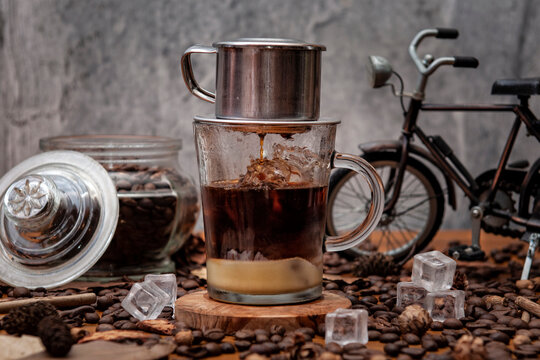 Kawa po wietnamsku z filtrem na szklance stojąca na stole wysypanym ziarnami kawy