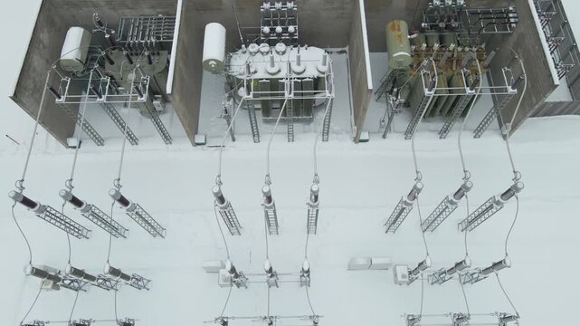 Top down start pulls back to unveil transformers, insulators, and pylons across a frost covered electrical switchyard.