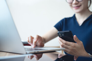 Happy asian business woman using smartphone, working on laptop computer at coffee shop or home office. Casual woman using smartphone and laptop browsing the internet 
