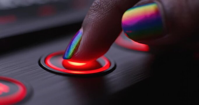 Close-up of a hand with rainbow nail polish pressing a button on a sleek device