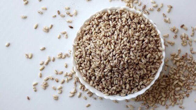 Top view of seasoned puffed rice (muri) in a white ceramic bowl on a white background. A healthy, organic snack and traditional Asian cereal, perfect for food industry and nutrition concepts