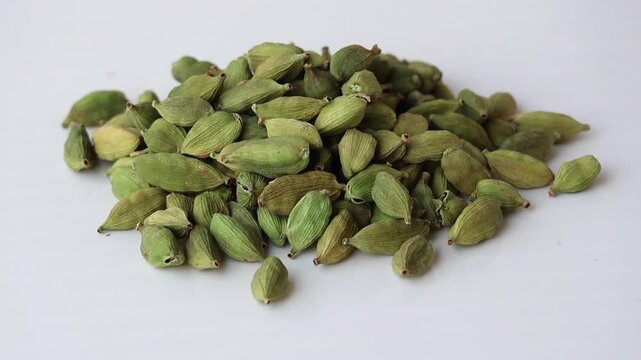 Fresh, high-quality green cardamom pods piled on white. Essential aromatic spice for masala chai, baking, and healthy herbal remedies. Clean studio footage for food and cooking concepts