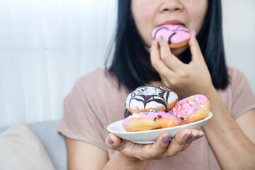 Young woman indulging in a plate of colorful sweet glazed donuts, concept of sugar addiction, unhealthy eating habits, craving desserts, and emotional binge eating at home