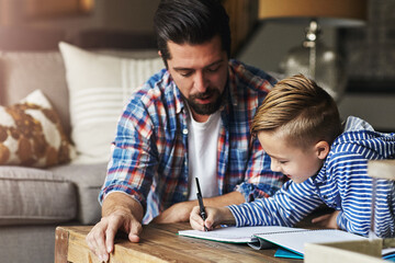 Writing, kid and father help with homework in home for learning support, language activity or study. Education, dad or child with book at table for handwriting practice, fine motor skills or guidance © BuyoutReese09/peopleimages.com