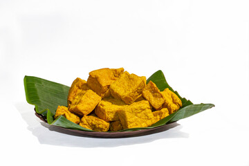 A full pile of traditional Indonesian fried yellow tofu (tahu kuning) served on a fresh green...