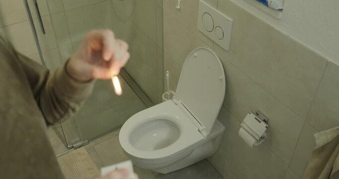 Realistic scene of a person lighting a match in a bathroom near a toilet to mask unpleasant odor, symbolizing everyday hygiene habits and improvised odor control.