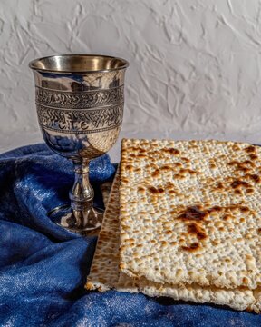Jewish Matzoh bread and silver kiddush cup on blue fabric for Passover holiday celebration greeting card with copy space for religious marketing and branding