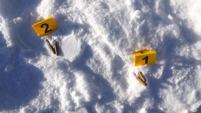Overhead move closes in on numbered markers, brass casings, and a visible footprint impressed in bright snow.