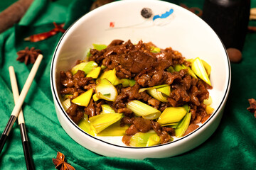 Inside a restaurant, a bowl of stir-fried beef and scallions sits on a green surface. Chopsticks are nearby. The dish is a traditional Chinese recipe, promoting healthy eating. © Aleksandr