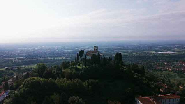 Aerial view of Montevecchia Italy showcasing the Sanctuary of the Madonna del Carmelo perched atop a tree-covered hill The landscape overlooks the Lombardy region offering a scenic vista.