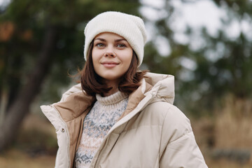 Outdoor portrait of a smiling woman in a beige jacket and knit sweater, wearing a white beanie, in a chilly park with soft natural light. © SHOTPRIME STUDIO