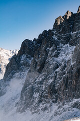 Sharp rocky mountain peak covered with snow against a clear blue sky. High altitude alpine landscape in winter.