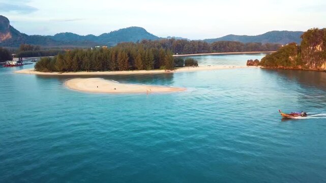Stunning aerial footage of a traditional Thai longtail boat sailing through turquoise waters at Nopparat Thara Beach, Krabi, during golden hour.