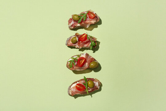 Tasty canapes with jamon, olives and tomatoes on green background