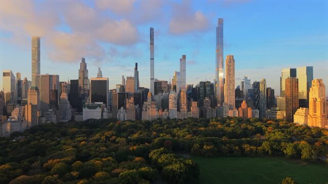 Aerial drone view of Manhattan skyline rising above Central Park in New York City, New York during golden hour with warm sunlight, long shadows and calm atmosphere.