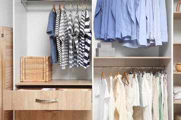 Wardrobe with hanging clothes and open drawer in room