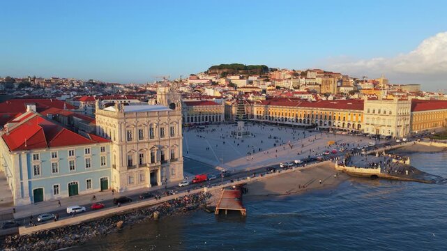 Drone footage of Lisbon historic Praca do Comercio near the river captures daily city movement, classic facades and open urban space in warm daylight