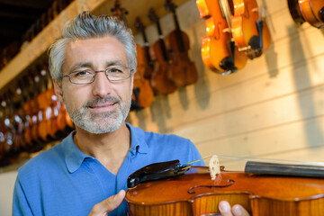 mature violin maker while testing the violins in his laboratory © auremar