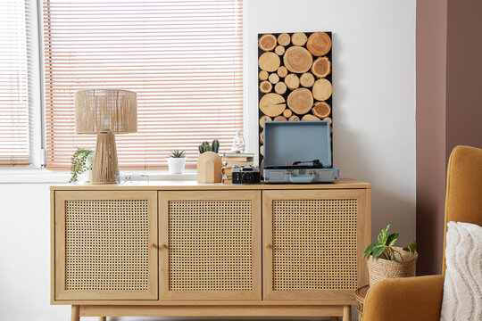 Books, record player and lamp on chest of drawers near window in living room, closeup