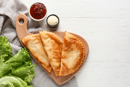 Board with tasty chebureks, fresh lettuce and sauces on white wooden table