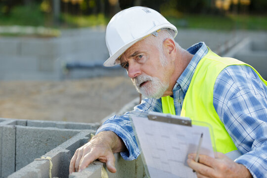 aged man holding cardboard inspect concrete wall