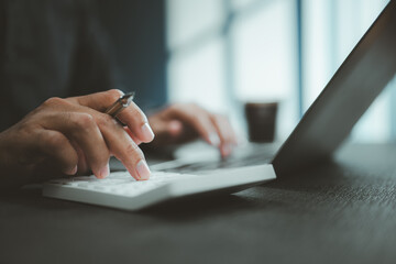 Person Using Calculator and Laptop for Financial Calculation in Office