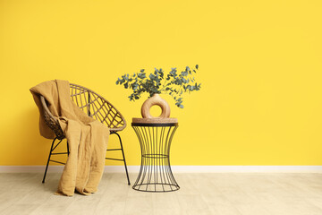 Chair and coffee table with eucalyptus branches in vase near yellow wall in room