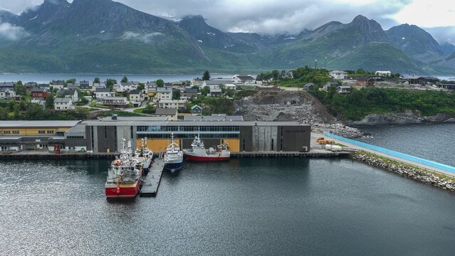 12 july 2025, Hus&oslash;y, Norway. Aerial, drone view of harbor in  village Husoy and island in &Oslash;yfjorden fjord during sunset. Ships, fishing industry, packhouses. Beautiful nature, mountains surrounding fj
