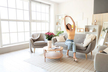 Young woman sitting on sofa with roses in vase at home