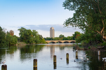River view with tall building in city background and bridge connecting two banks under clear sky during daytime .