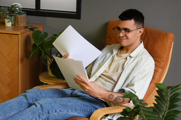 Male author with paper sheets lying in armchair at home