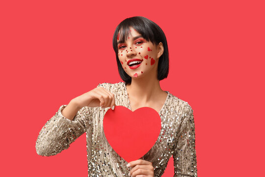 Beautiful young young woman with creative makeup for Valentines Day and paper heart on red background