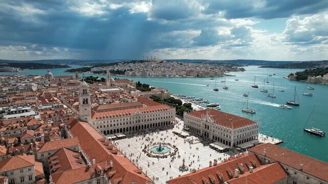 Aerial view of bustling historic city square and harbor with boats.
