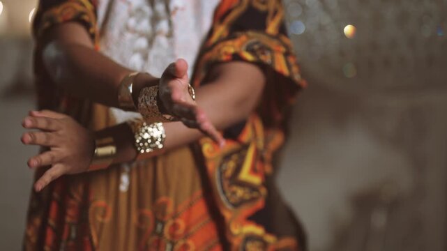 Luxury golden bracelets on hands of beautiful female dancer, african aesthetic. Closeup view of moving female hands, black lady dancing in luxury royal palace, ethnic collection of jewelry store
