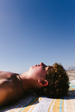 Teen boy with curly hair sleeping on beach with blue sky