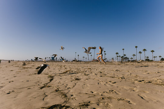Teenage woman running on sandy beach with blue sky